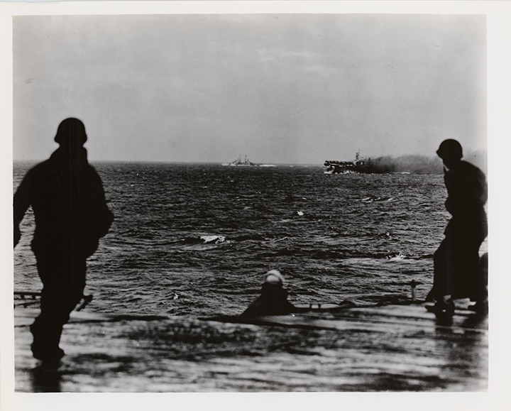 Three crewman on approaching ship view 4th USS Princeton (CLV-23) on fire east of Luzon as another ship appoaches